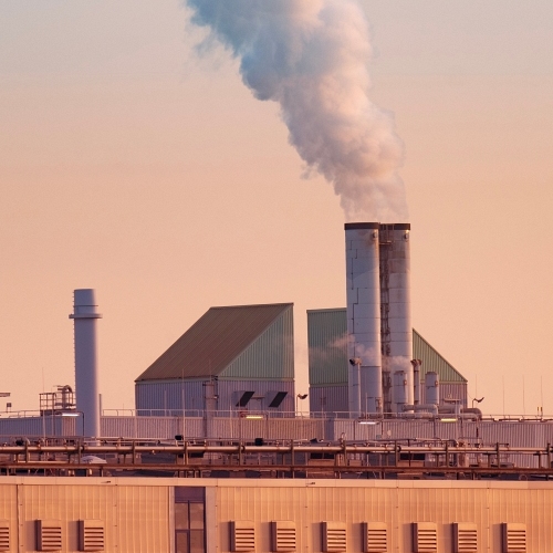 Ein Blick auf eine Fabrik, aus deren Schornstein bei Sonnenuntergang Dampf aufsteigt