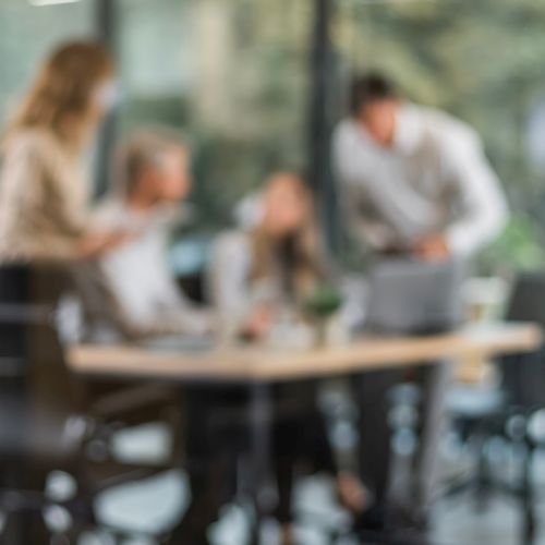 Vier Personen unscharf an einem Bürotisch in einer Besprechung.