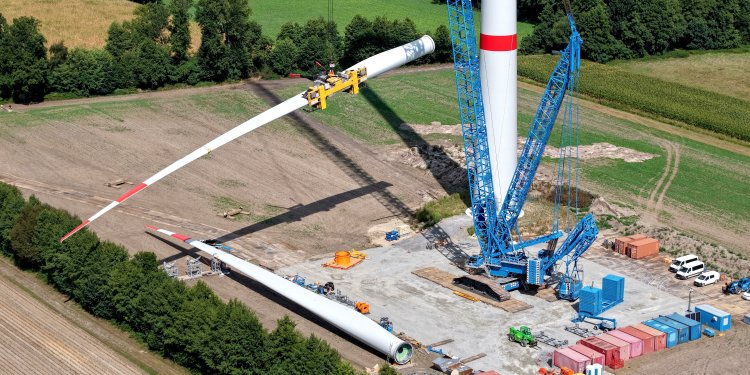 Riesiger Schwerlastkran zieht Windradflügel für eine neue Windkraftanlage hoch.